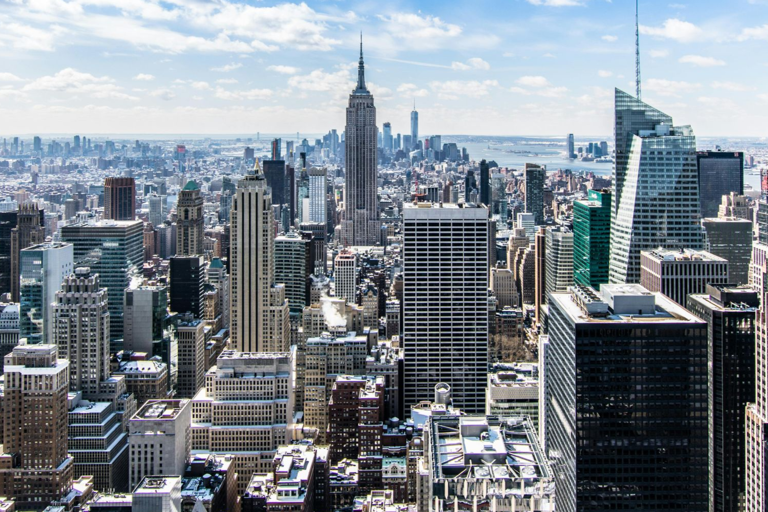 New York City skyline with the Empire State Building dominating the view under a bright blue sky.