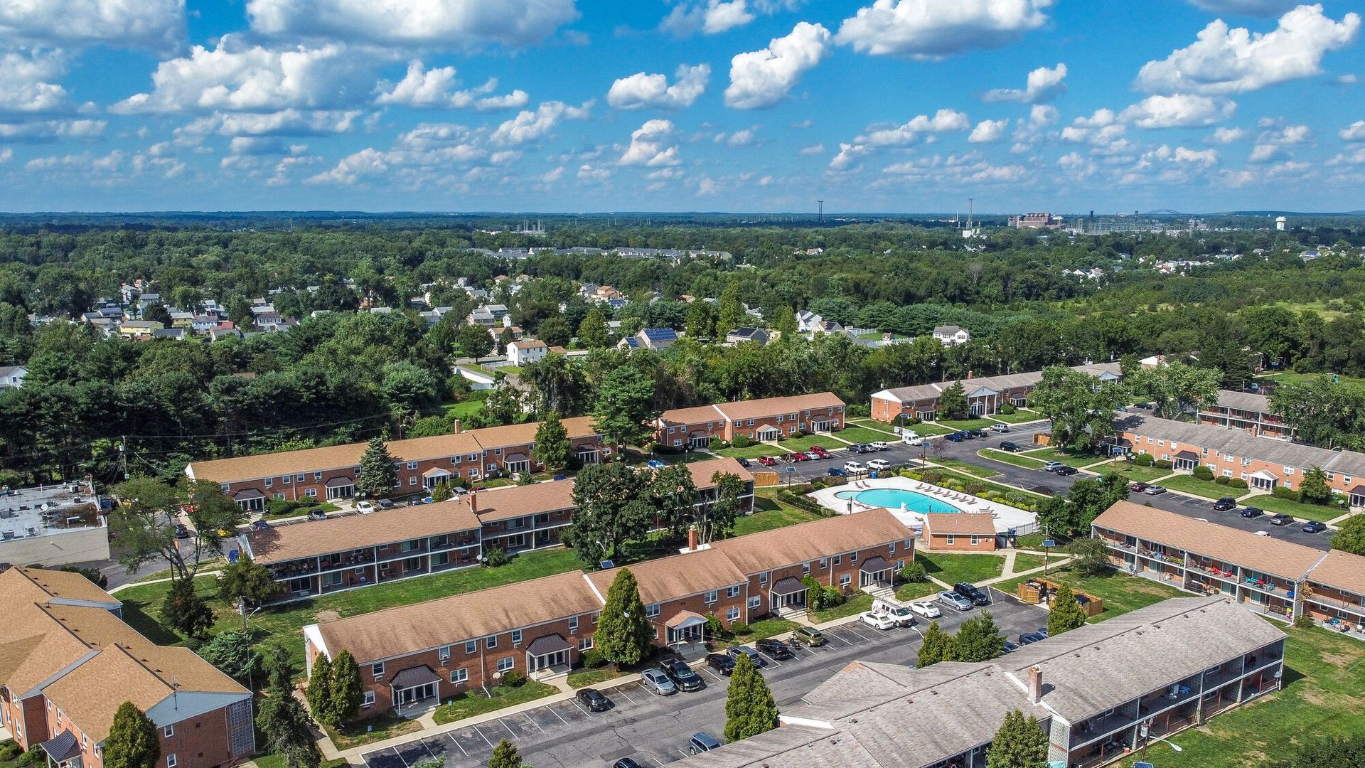 Aerial view of a large apartment community with brick buildings, a central pool, and parking.