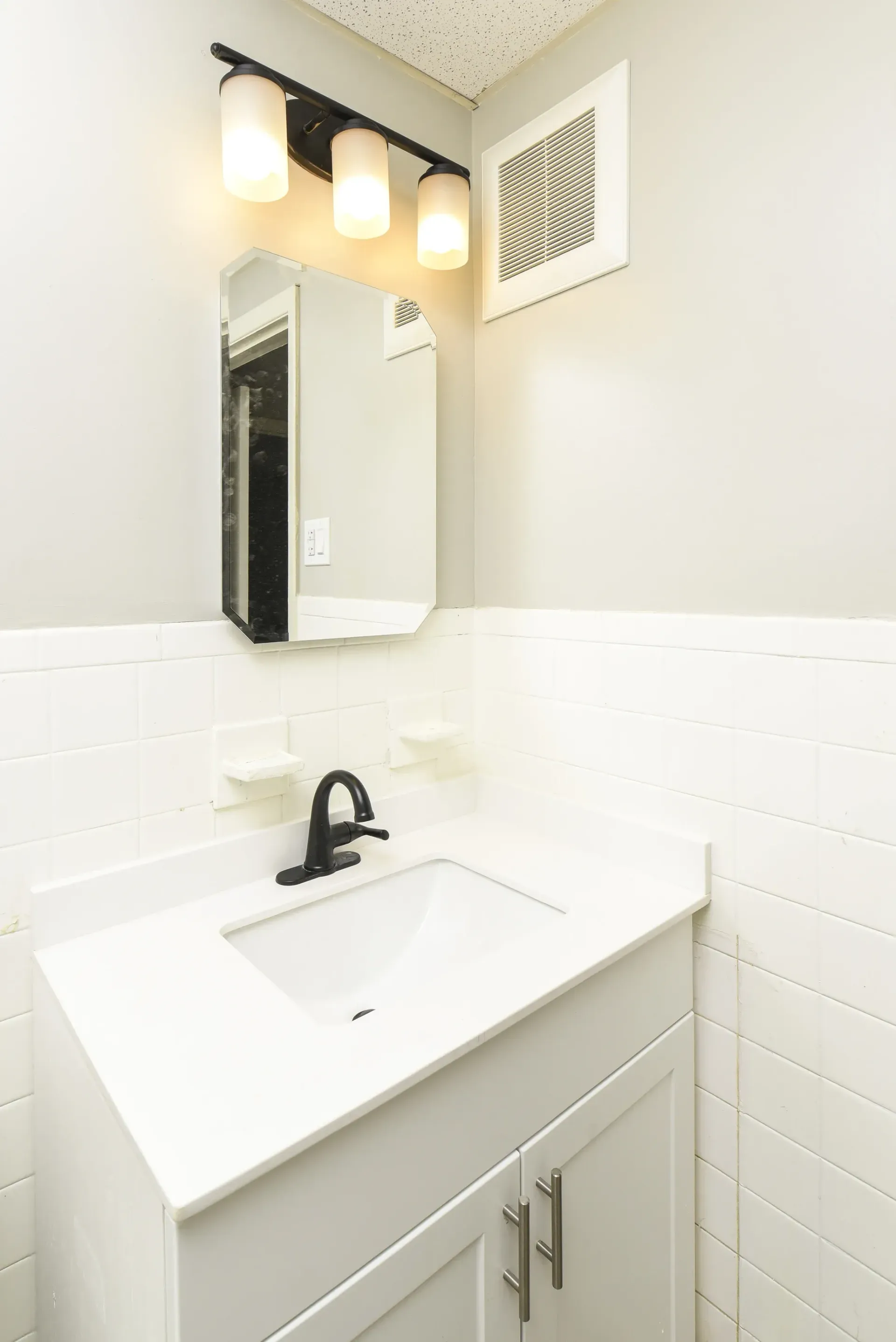 White bathroom vanity with sink, black faucet, mirror, and three-light fixture.