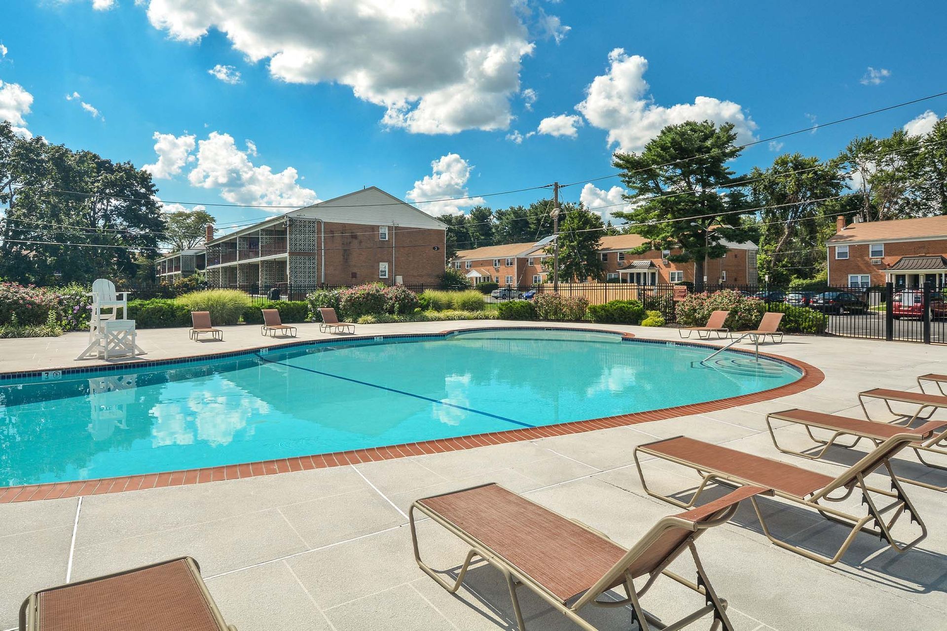 Outdoor apartment community pool with lounge chairs and landscaping.