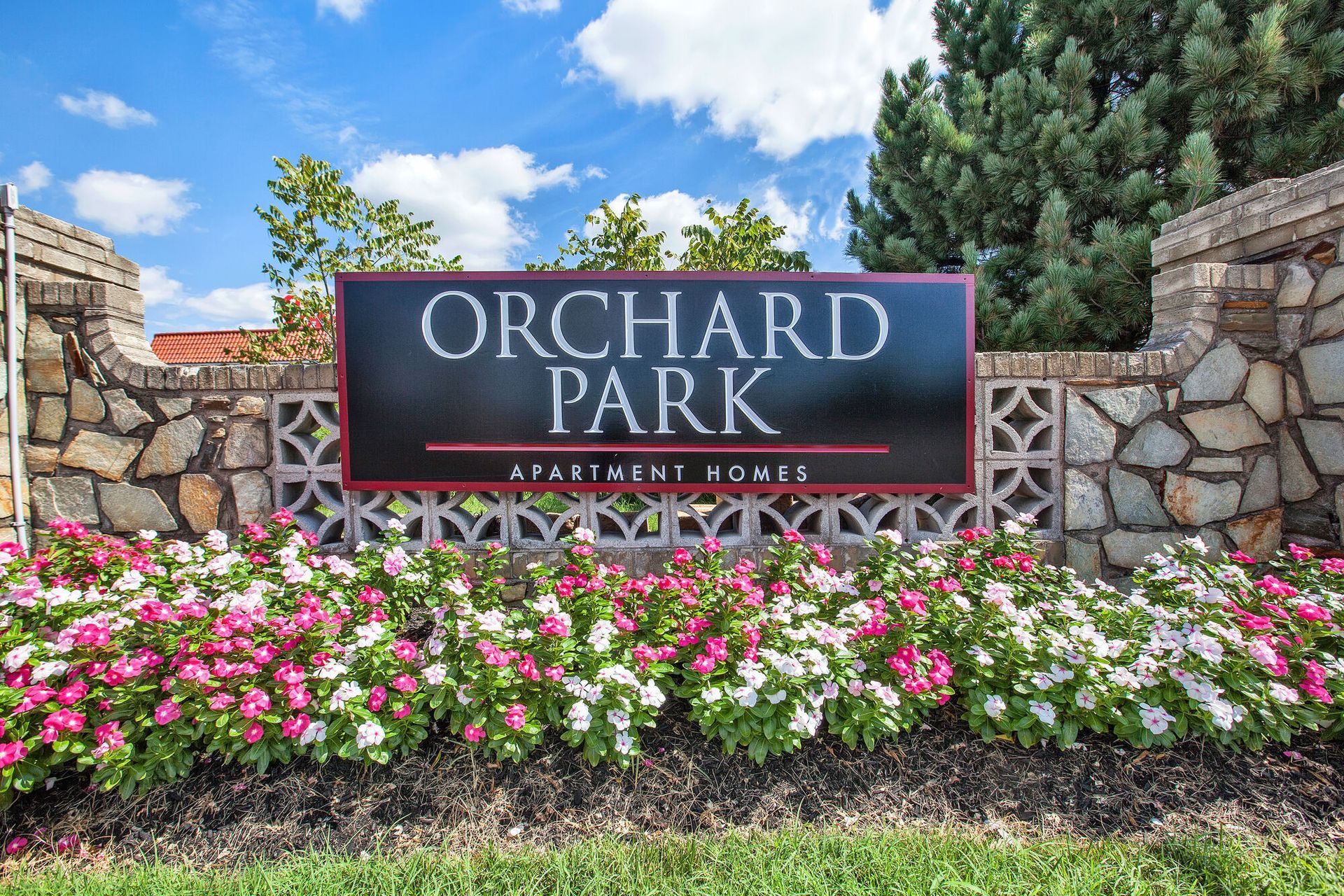 Exterior community sign for Orchard Park Apartment Homes with a stone wall and flowers.