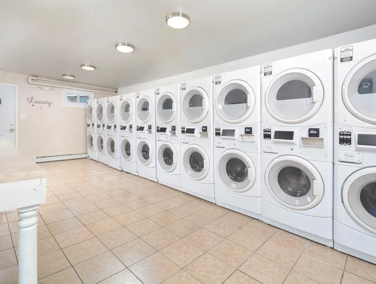 Communal laundry room with rows of front-loading washing machines along the wall.