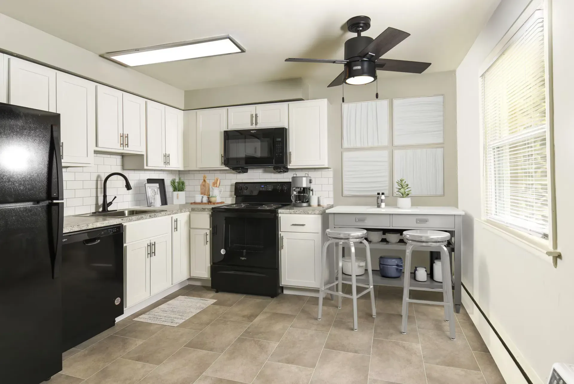 White kitchen in an apartment with black appliances, grey countertops, and a small breakfast bar with two stools.