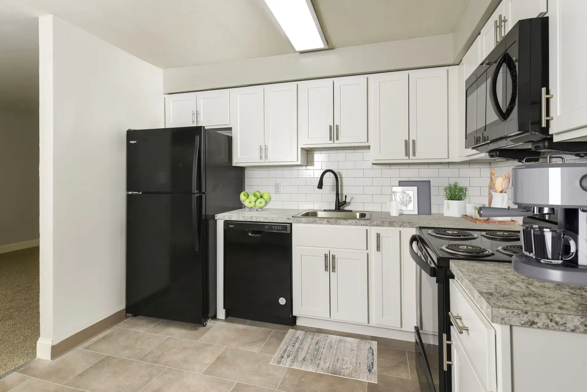 White kitchen with white cabinets, black appliances, and a black sink faucet.