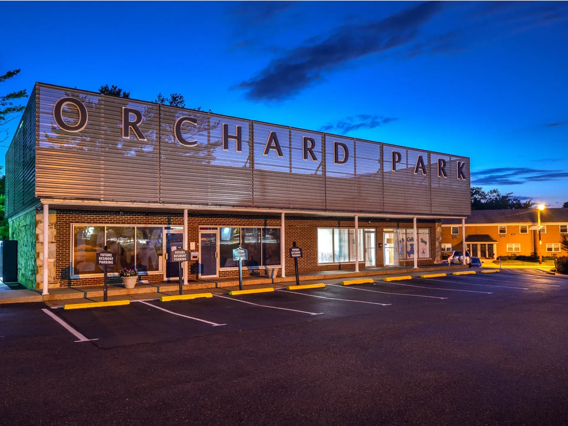 Exterior view of Orchard Park apartment community at dusk, brick building with signage and a parking lot.