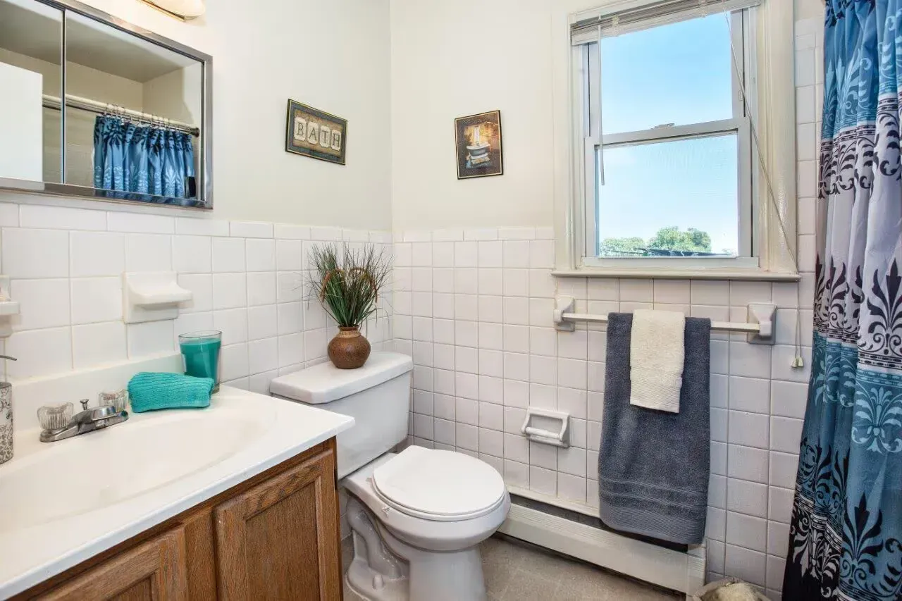 Bathroom in an apartment with sink, toilet, tiled walls, window, and blue towel.