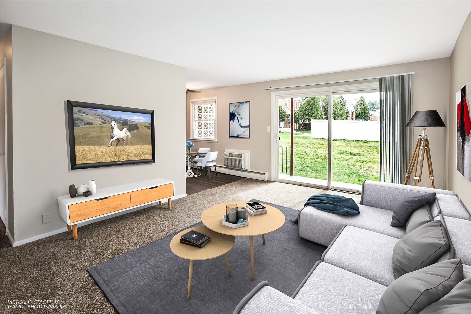 Living room in an apartment with a gray sectional, wall-mounted TV, and a sliding glass door to an outdoor area.