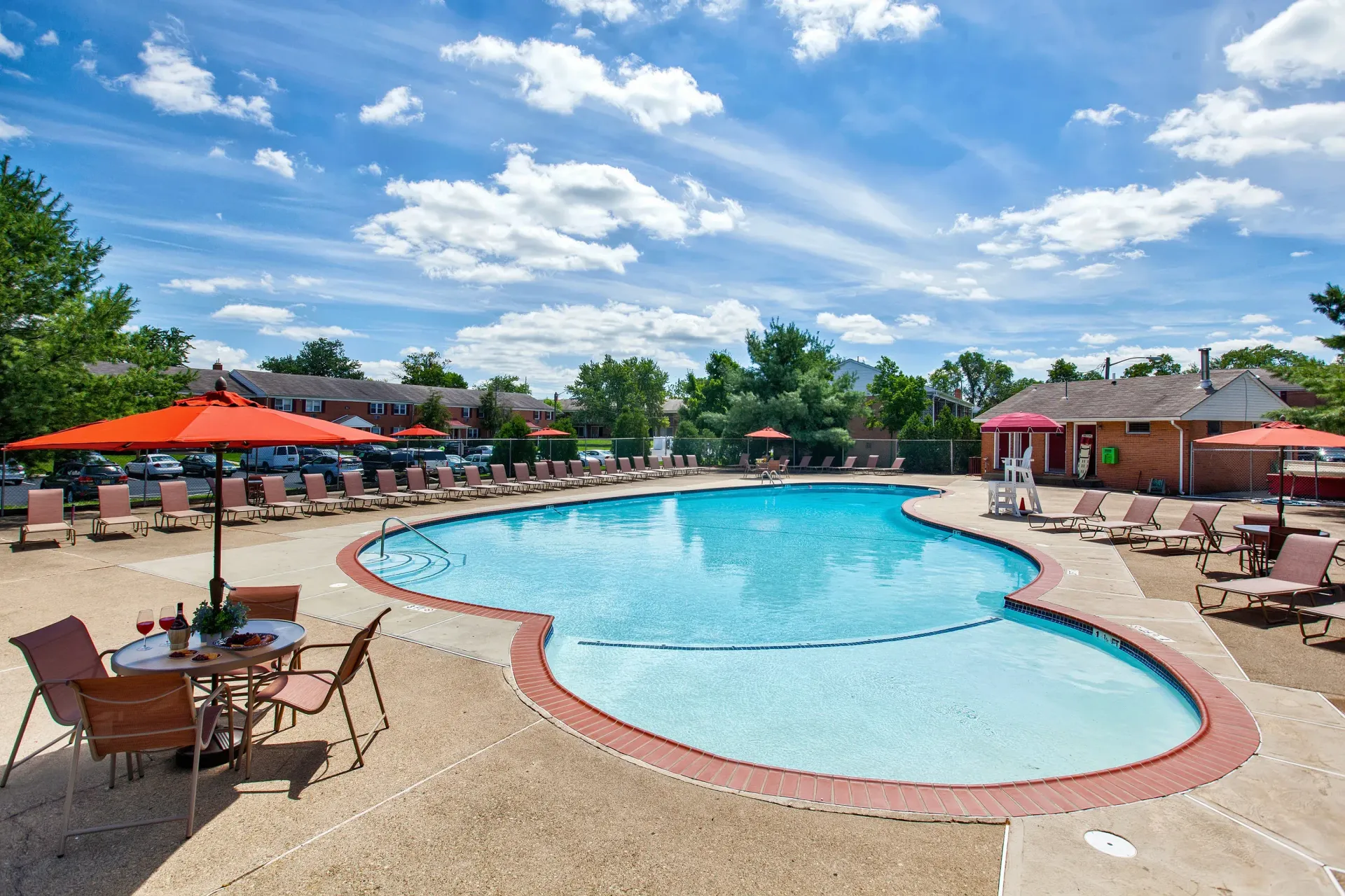 Outdoor community pool with curved shape, lounge chairs, and red umbrellas on a sunny deck.
