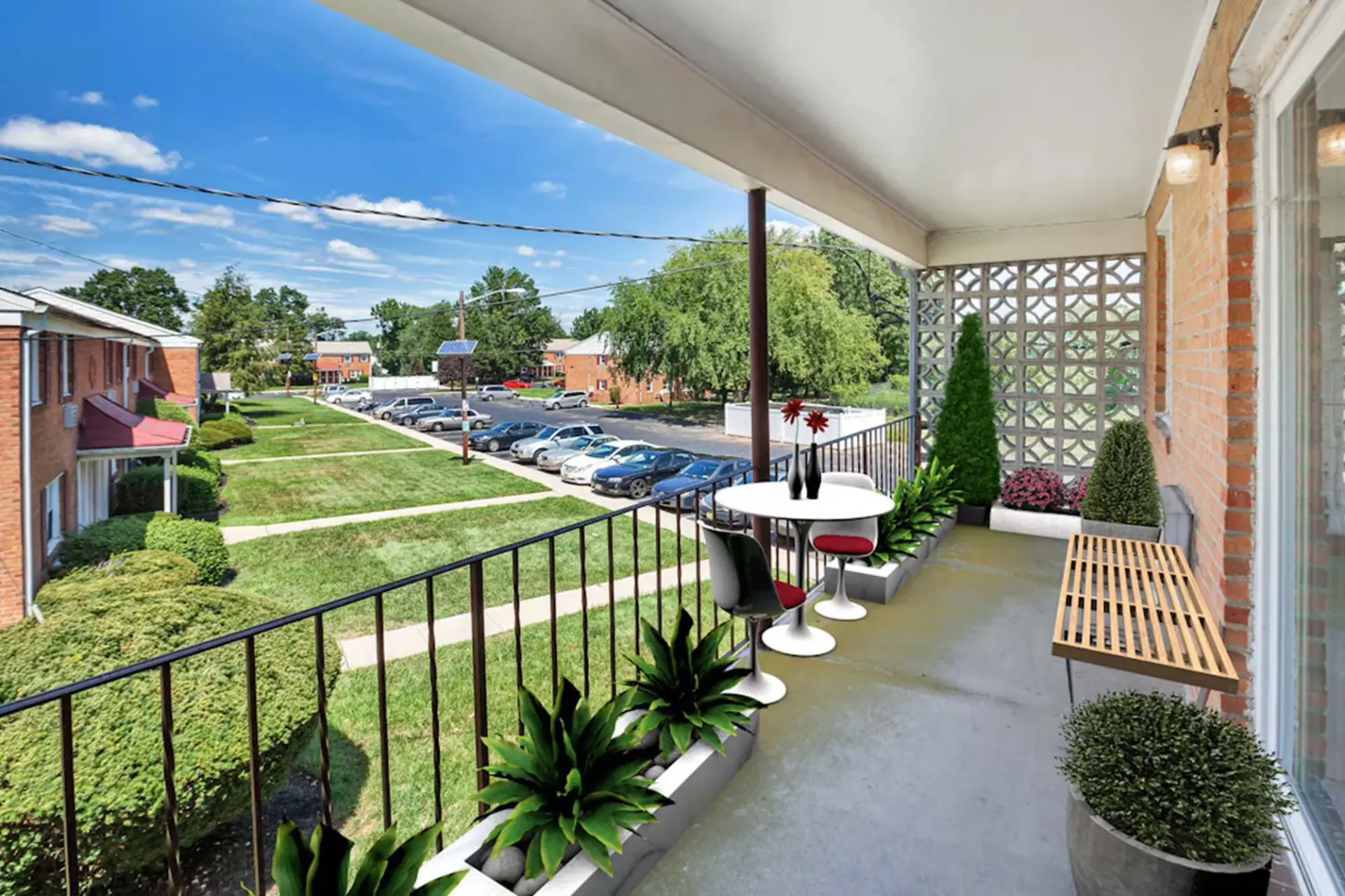 Balcony of an apartment with a small round table and chairs overlooking a grassy courtyard and parking.