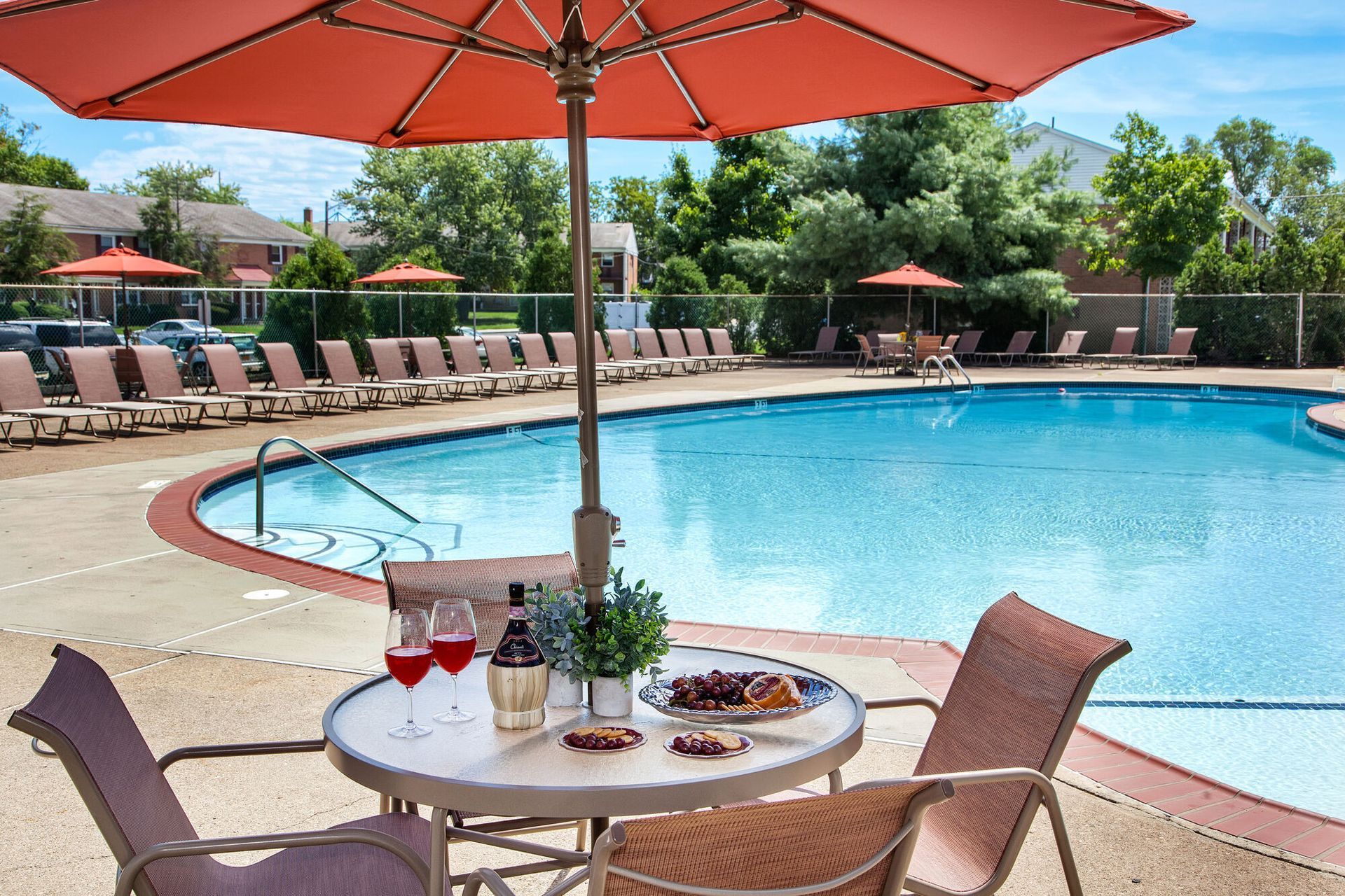 Outdoor pool area with lounge chairs, red umbrellas, and a table set with drinks.
