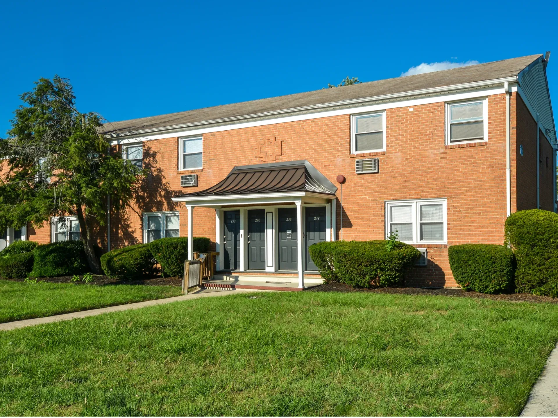 Brick apartment building exterior with a small covered entry and green lawn.