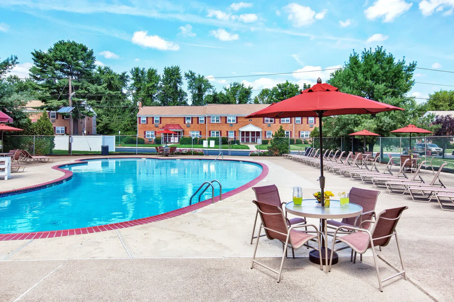 Outdoor apartment pool area with red umbrellas and lounge chairs.