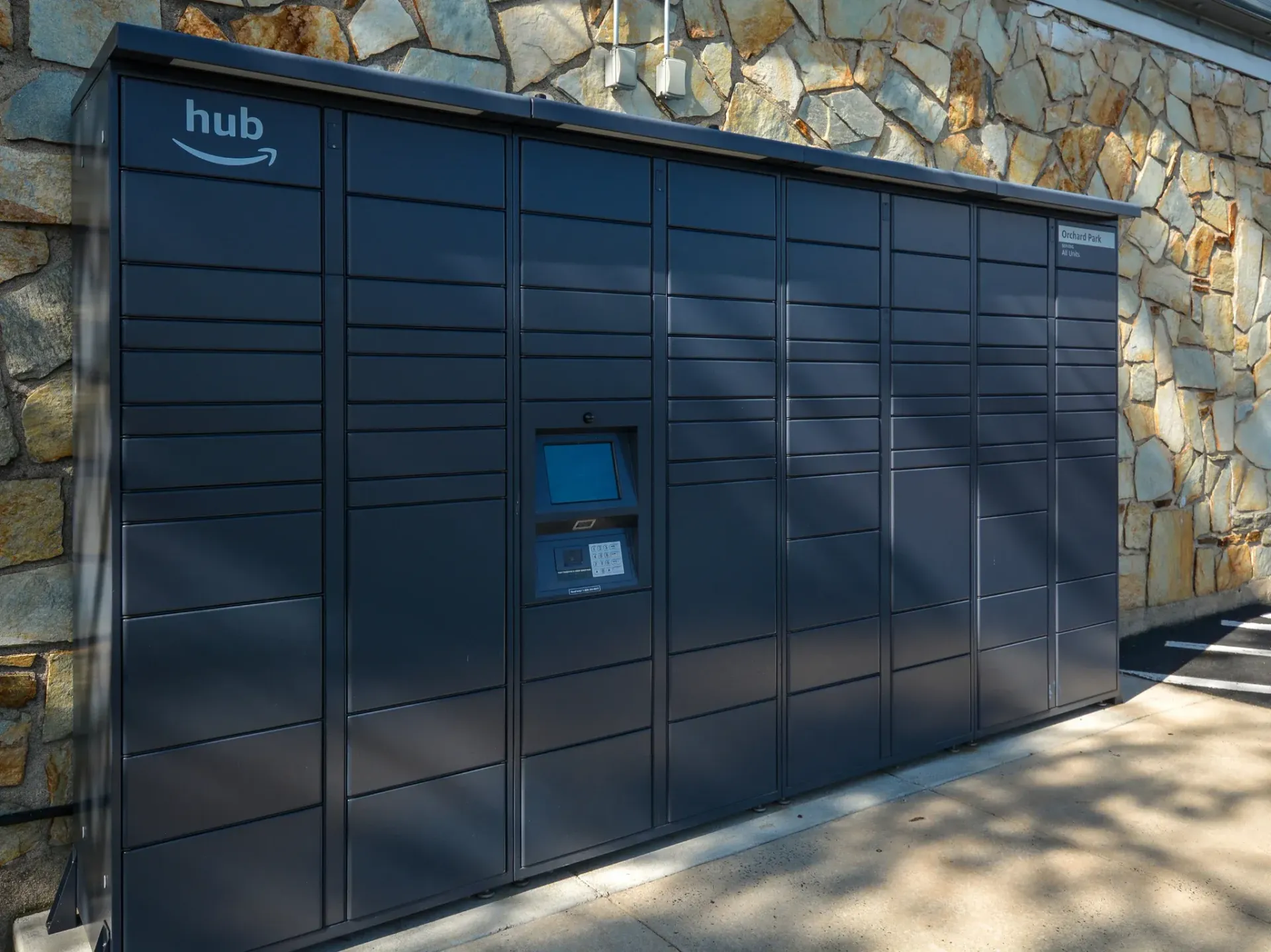 Row of dark blue parcel lockers against a stone wall at an apartment community.