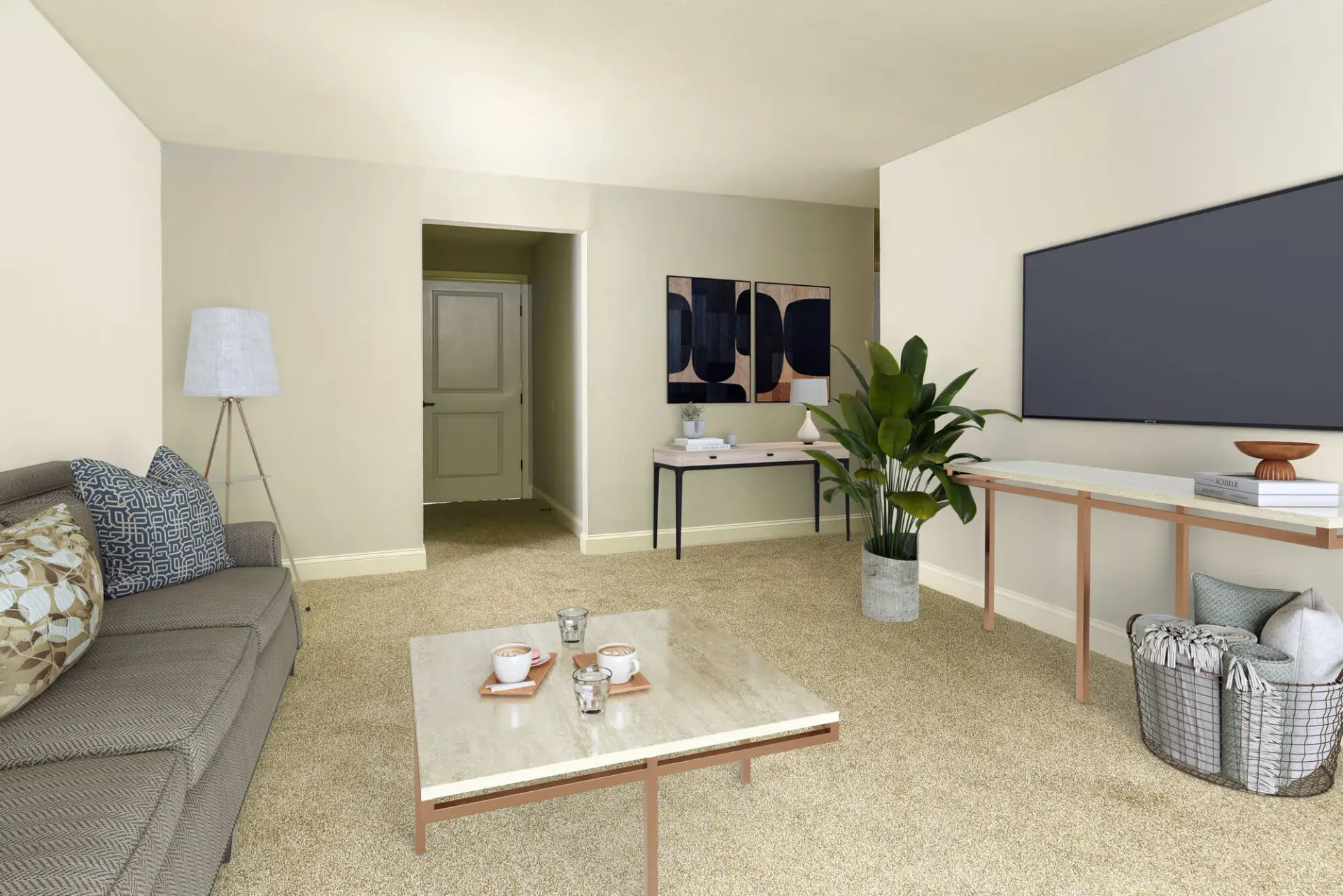 Living room in an apartment with a gray sofa, coffee table, plants, and a large wall-mounted TV.