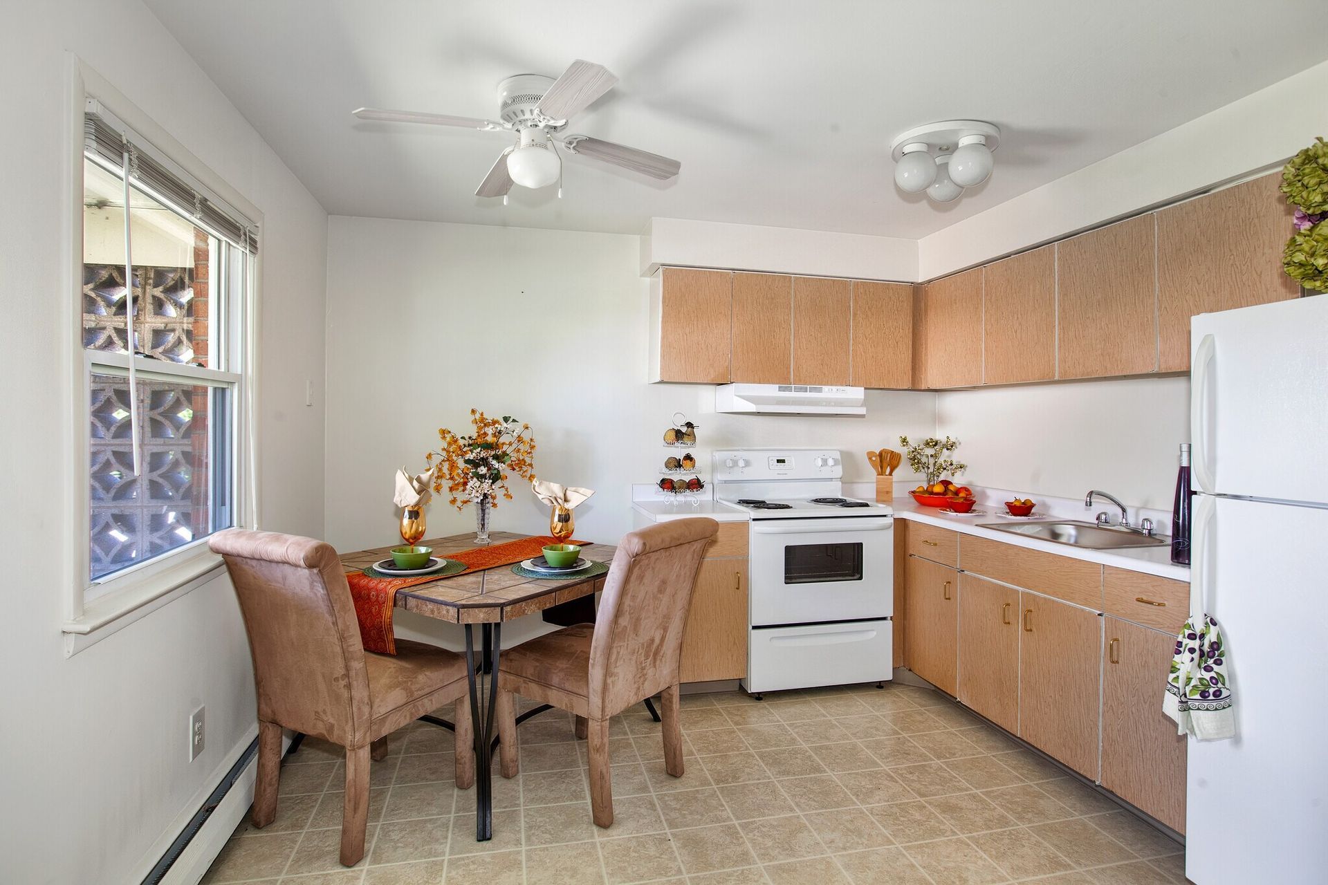 Apartment kitchen with light wood cabinets, white appliances, and a small dining table by the window.