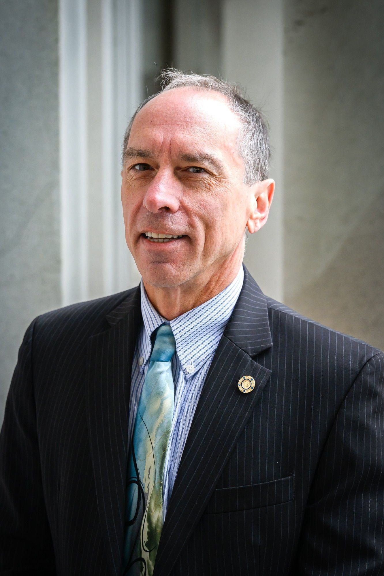 Man in suit and tie, smiling, standing outdoors near a building with columns.