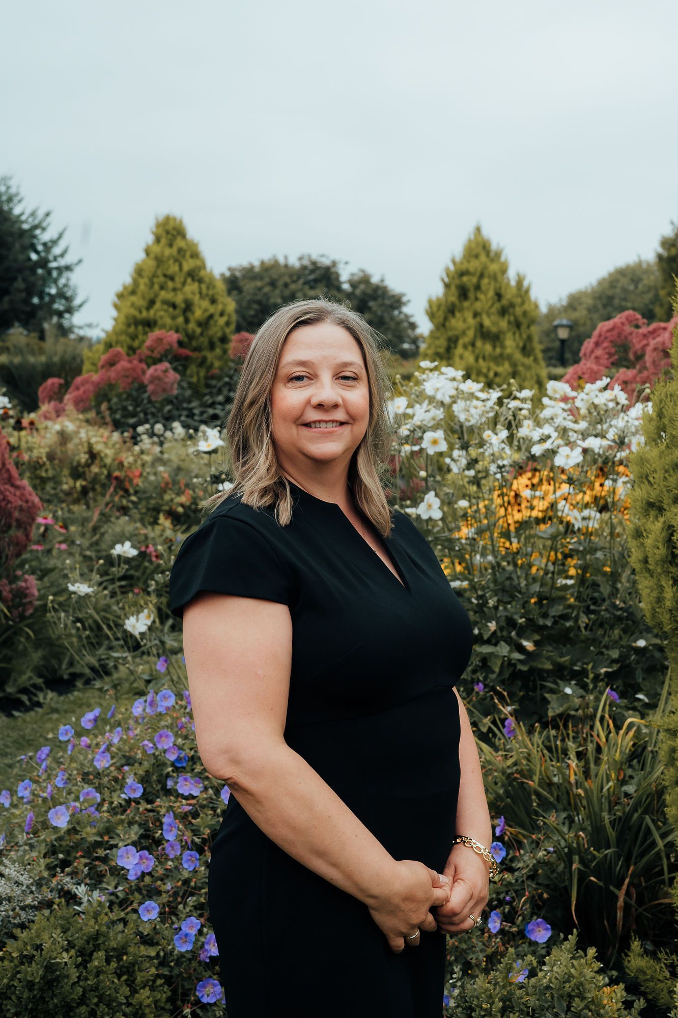 Woman in black dress stands in front of a colorful flower garden.