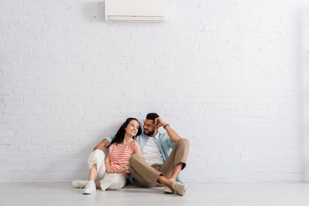 Couple Sitting Under Air Conditioner —  HVAC Systems in Dubbo, NSW