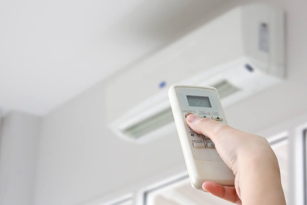 person using a remote to adjust a wall-mounted commercial air conditioner in a Dubbo office