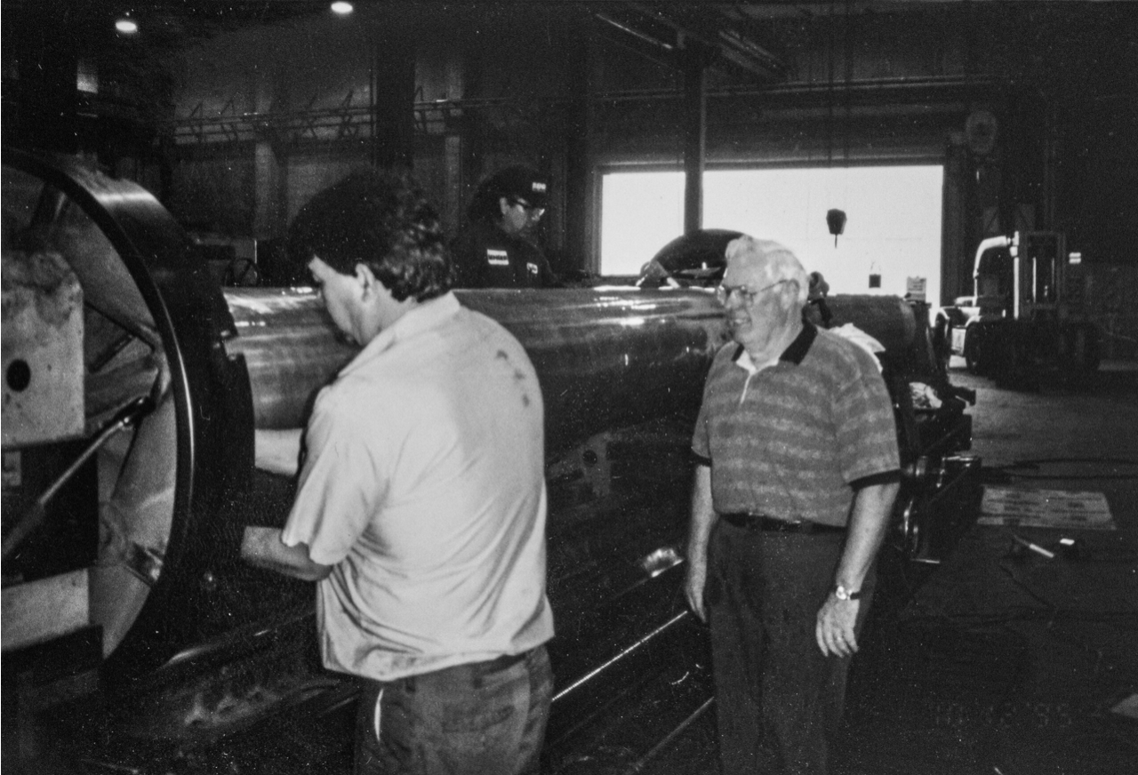 Two men working on machinery inside a workshop, one observing.
