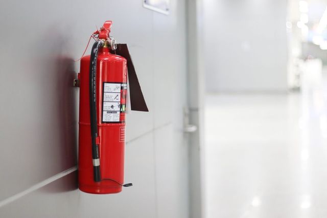 Red fire extinguisher mounted on a wall in a bright hallway.