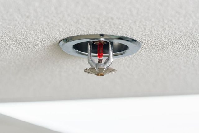 Ceiling sprinkler head with a red glass bulb mounted in a white textured ceiling