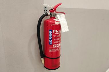 Red fire extinguisher mounted on a wall with a black hose and inspection tag