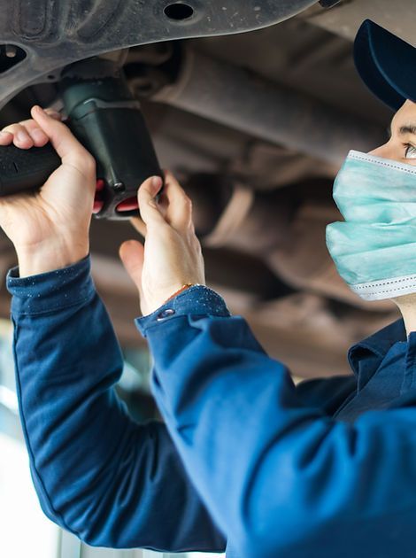 A man wearing a mask is working on a car with a drill.