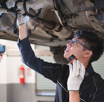 A man wearing glasses is talking on a cell phone under a car