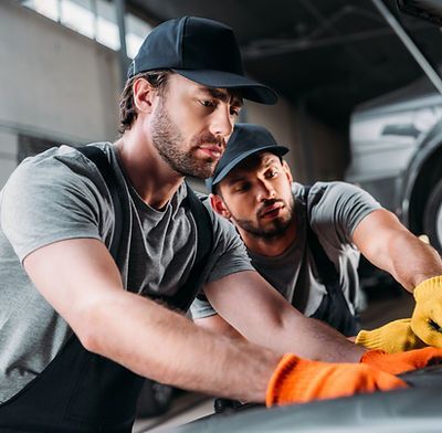 Two men are working on a car in a garage.