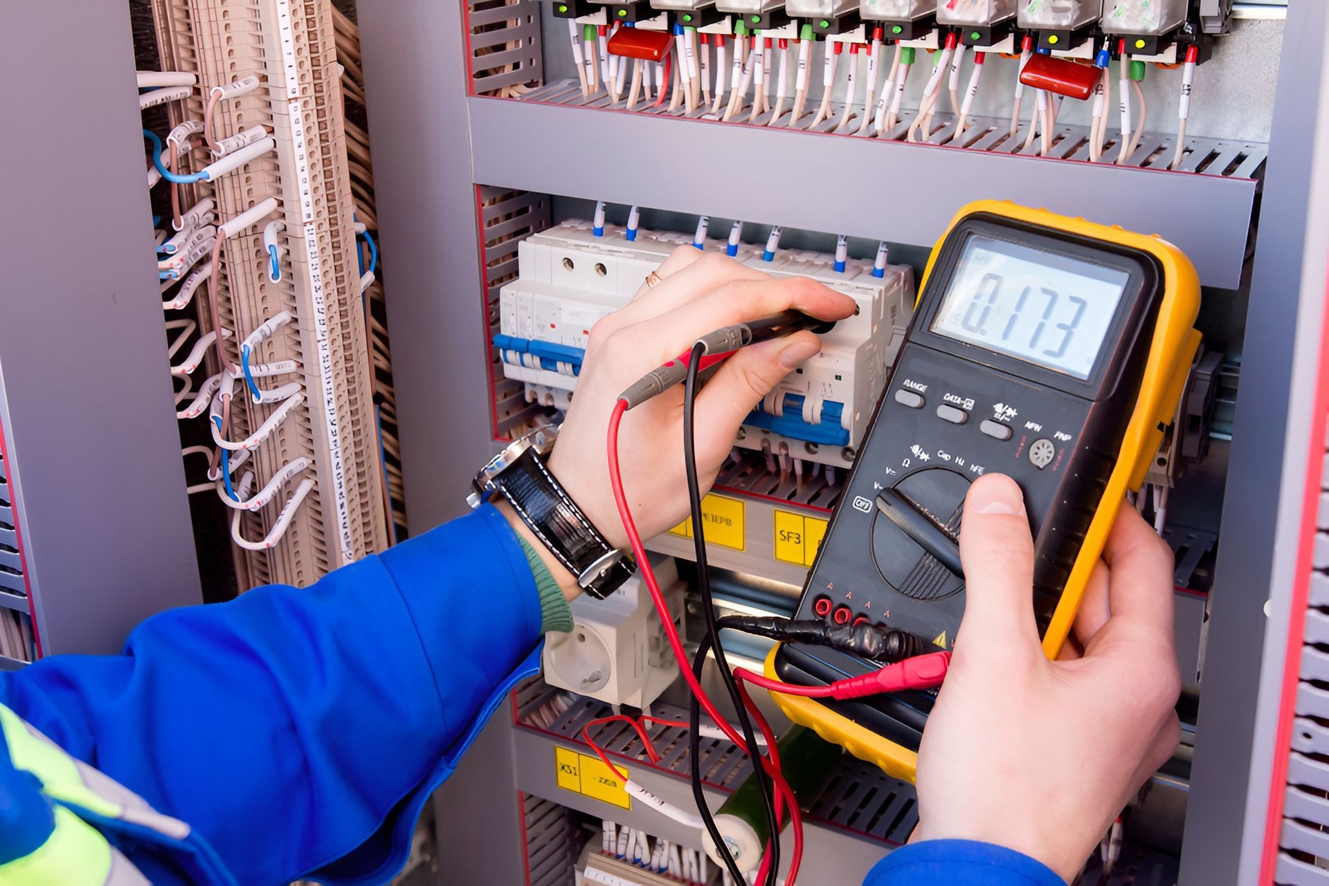 Electrician In Blue Uniform Tests A Control Panel With A Multimeter — Fry Electrical In Budgewoi, NSW