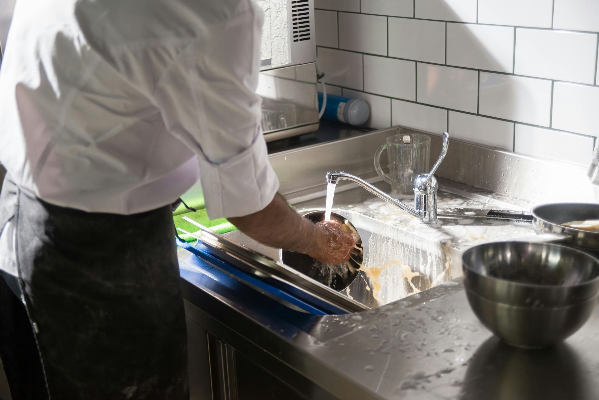 A man is washing dishes in a kitchen sink.