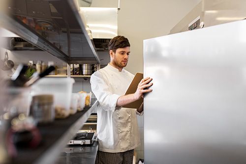 A chef is looking at a clipboard in a kitchen.