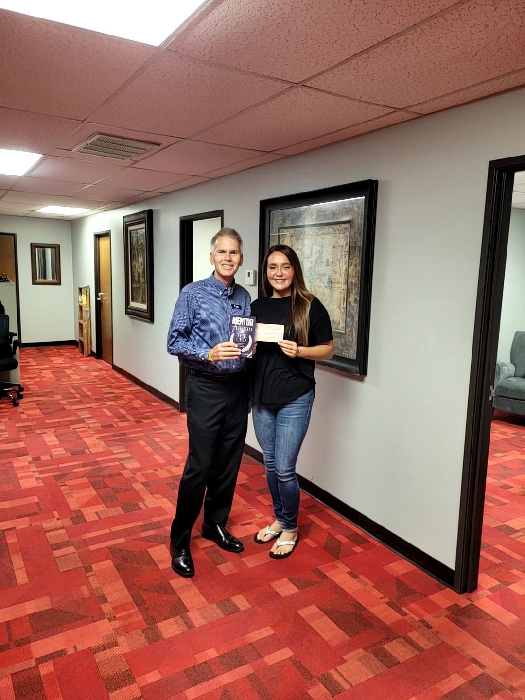 A man and a woman are standing in a hallway holding a check.