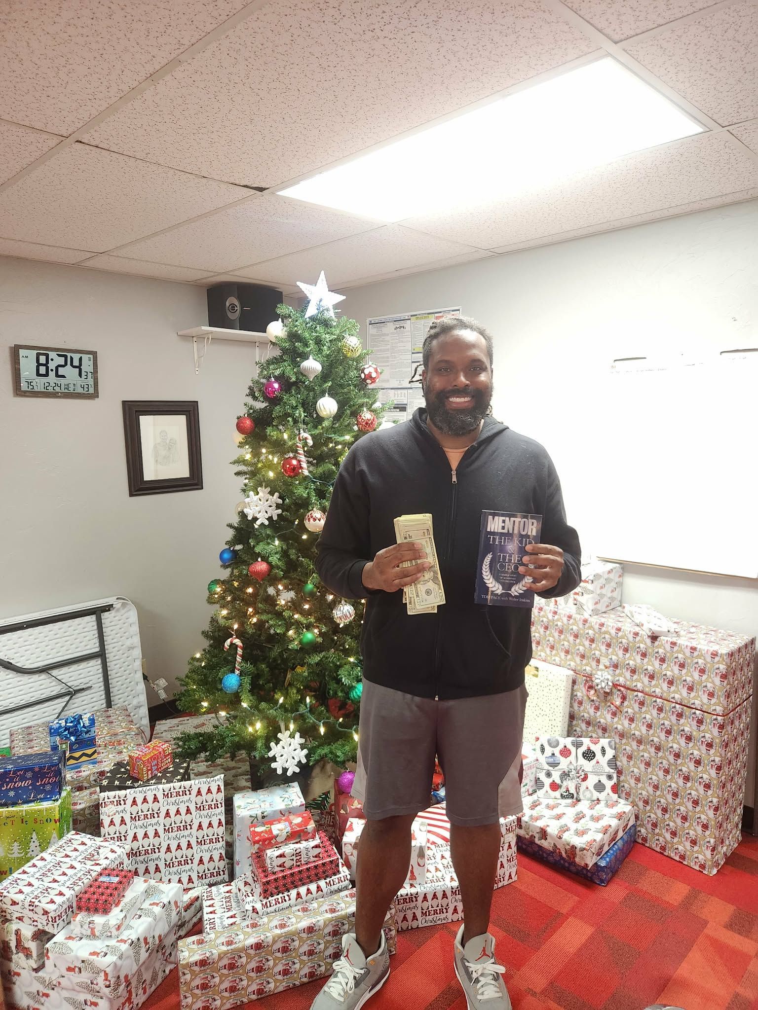 Man holding cash and a book, smiling in a room with Christmas tree and wrapped presents.
