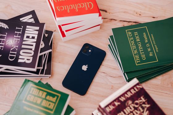 A red book titled alcoholics anonymous is surrounded by other books and a cell phone.