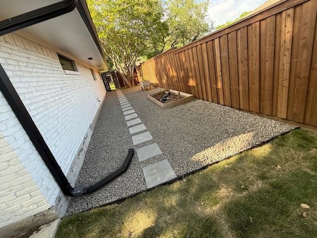 Person installing a drainage pipe in a trench, filled with gravel, in a yard.