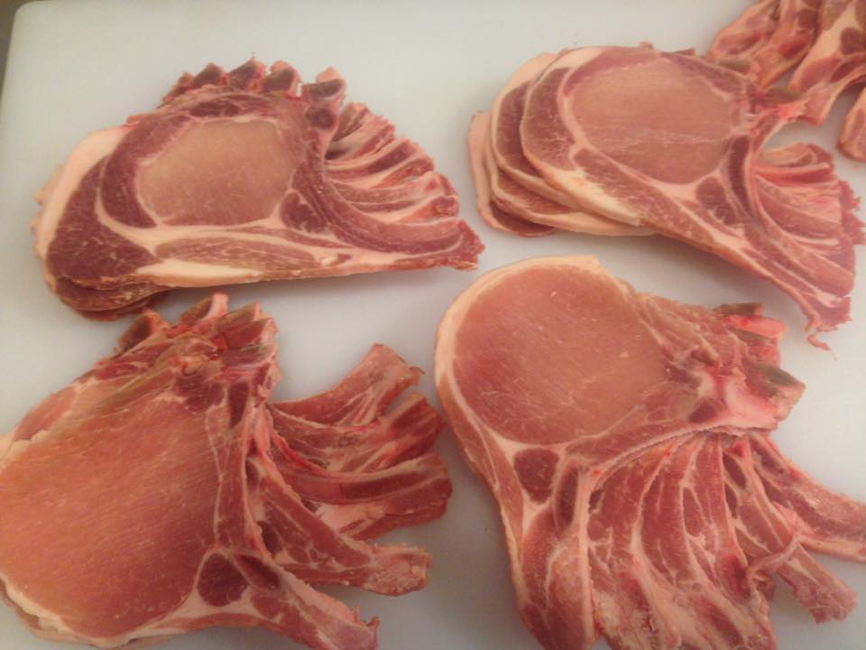 Four pieces of raw pork chops are sitting on a white cutting board.