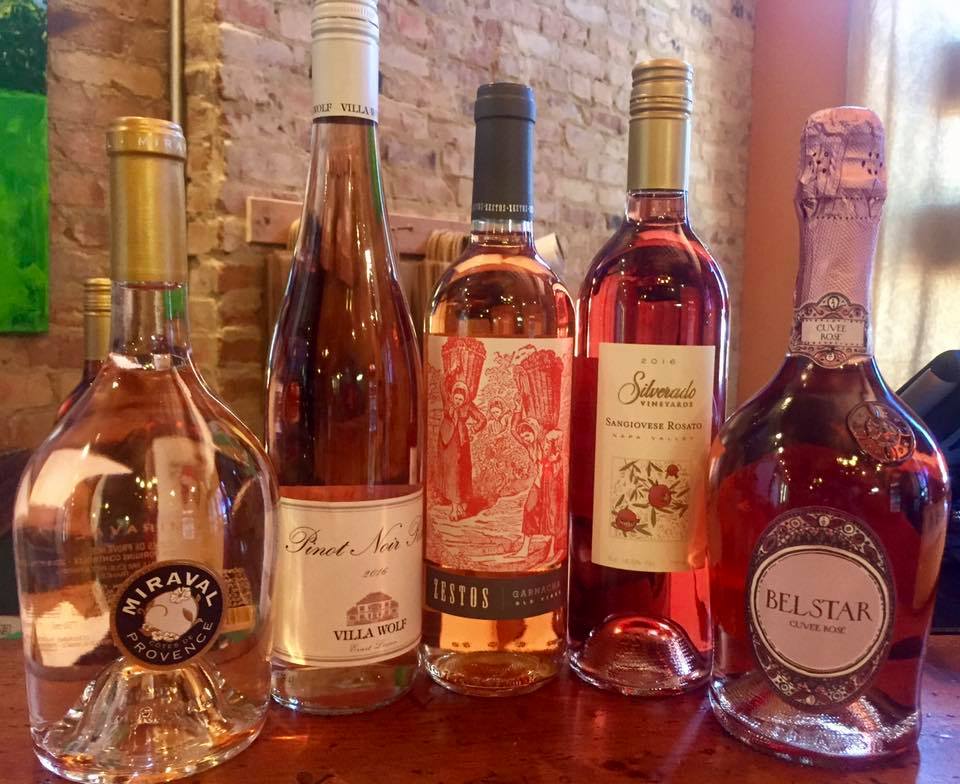 Five bottles of pink wine are lined up on a table