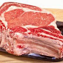 A large piece of raw beef is sitting on a plastic tray on a wooden cutting board.