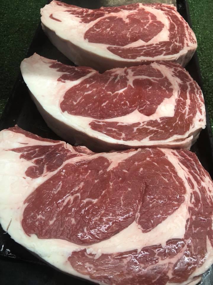Three steaks are sitting on a black tray on a table.