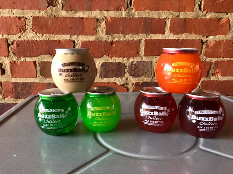 Several jars of buzzballs are on a table in front of a brick wall