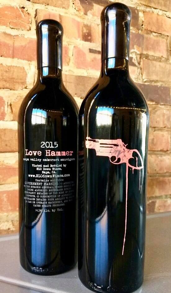 Two bottles of wine are sitting next to each other in front of a brick wall.