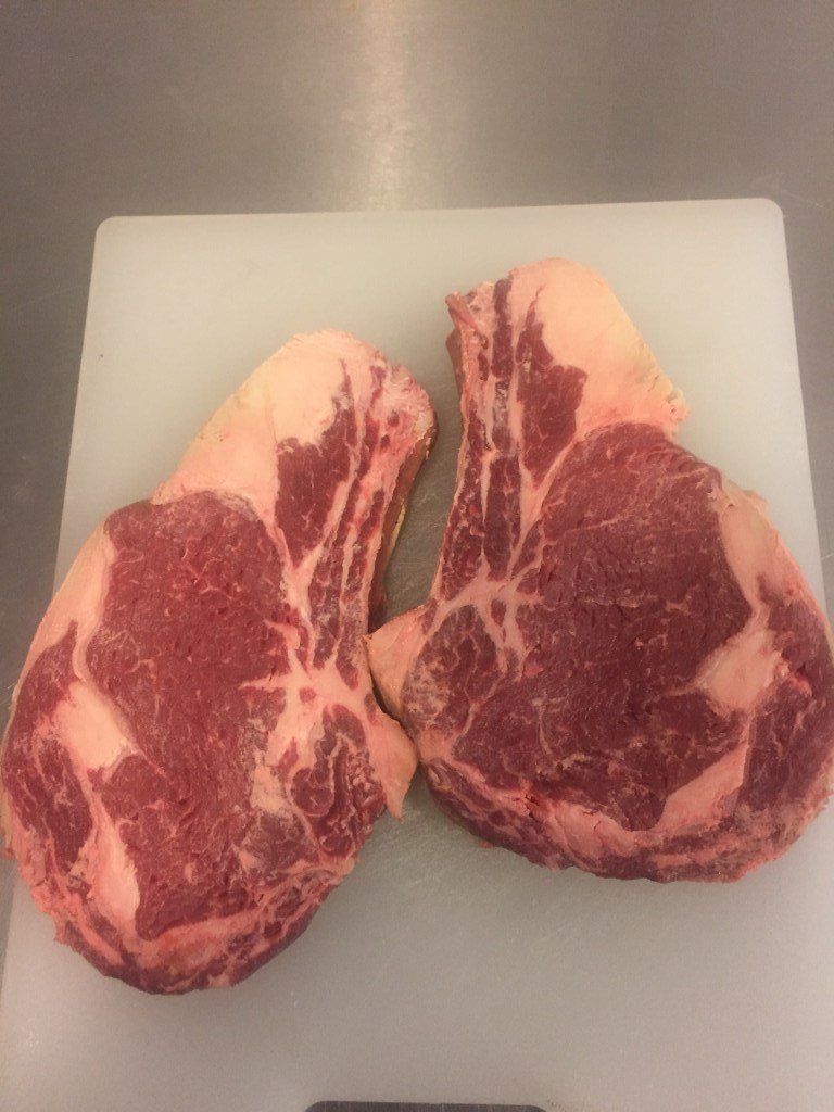 Two raw steaks are sitting on a white cutting board.