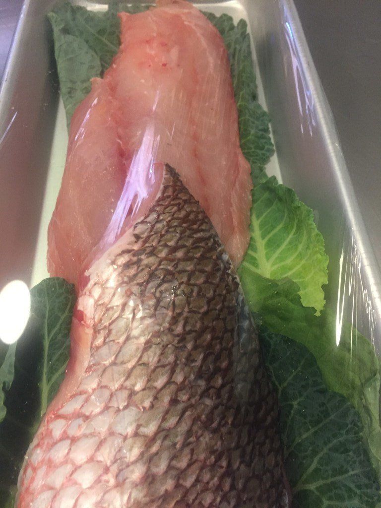 A fish is sitting on top of lettuce leaves in a tray.