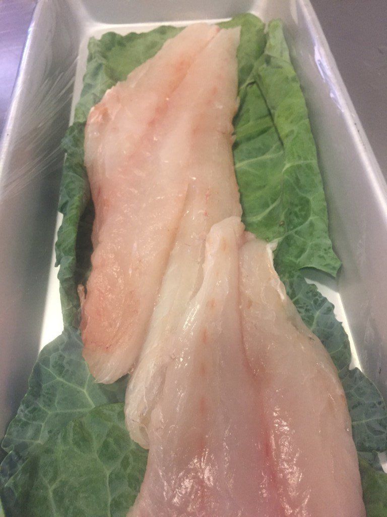 Two pieces of chicken breast are sitting on top of lettuce leaves in a tray.