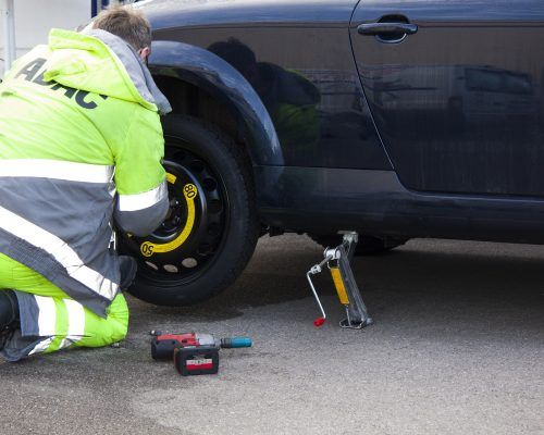 A man is changing a tire on a black car.