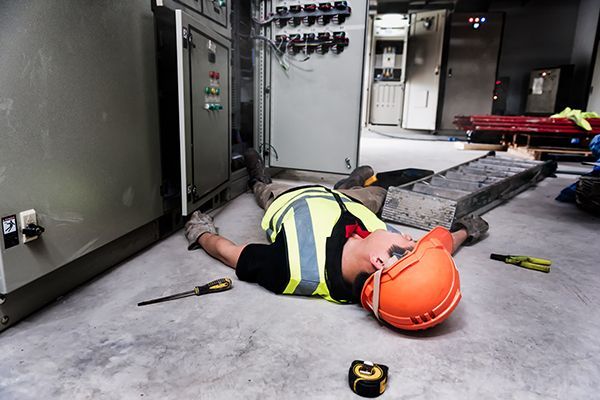 Worker in orange hard hat lies on factory floor beside industrial equipment.