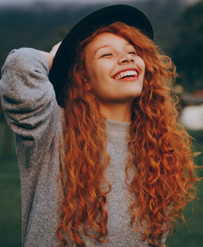A woman with red curly hair wearing a stylish hat.