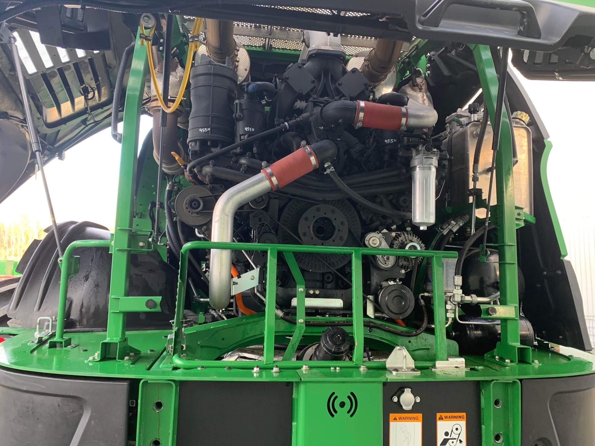 Le moteur d’un tracteur vert est représenté avec le capot ouvert.